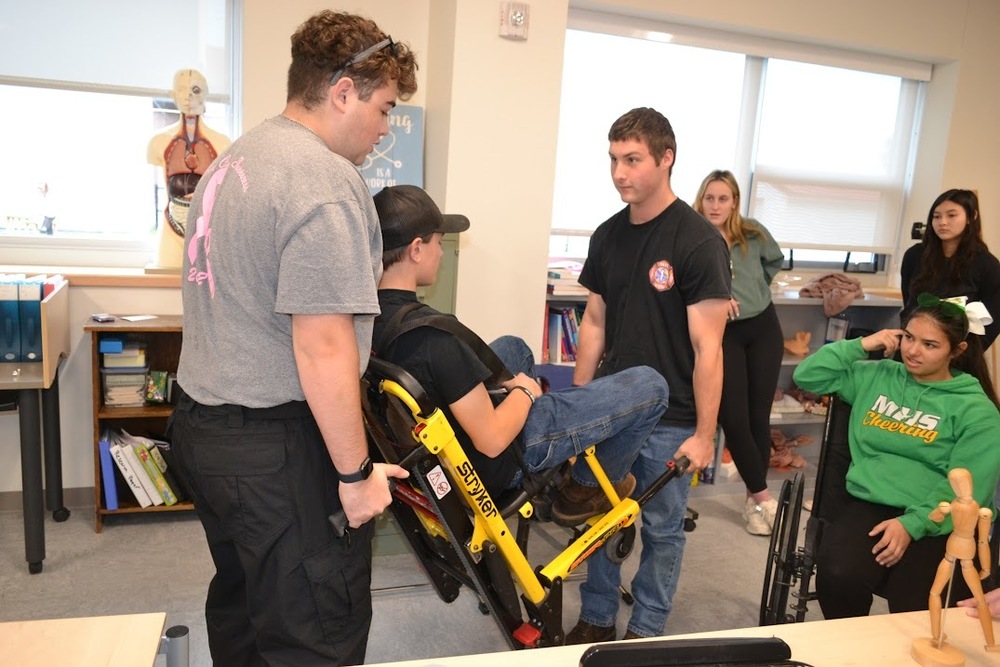 Students in Sanford Regional Technical Center's Health Occupations program move from classroom learning labs to real hospital floors, developing both the technical skills and compassionate caregiving approach needed to become Certified Nursing Assistants. The one-year course provides a rigorous foundation for students interested in healthcare careers. The curriculum satisfies requirements to become registered Certified Nursing Assistants in Maine upon successful completion and passing the Registry exam. Students learn to care for patients and residents in long-term care, skilled nursing, and rehabilitation settings, covering anatomy system by system along with common medical conditions. Beyond the technical training, instructors Shawnda Williams and Kelly Romagnoli emphasize what Williams calls the "Art" of caring – teaching students to provide respectful, dignified care to people during some of their most stressful moments. "We take great pride in developing these students into the health care professionals we would like to have care for us and our own family members and loved ones," Romagnoli said. "It is a joy to watch. I also enjoy watching them blossom and become the professionals we would like to work with on our team." Students begin by developing proficiency in the classroom learning lab, mastering basic safety and caregiving skills. Once they demonstrate readiness, they practice and perfect skills like hygiene, feeding, bathing, skin care, and assisting with patient mobility at Summer Commons and Pinnacle Health and Rehab in Sanford. Students complete a minimum of 40 hours of direct care under the instructors' supervision and the nursing teams at these facilities. For Bella Garneau, a junior at Sanford High School, the program has been a long-anticipated opportunity. "I had been interested in taking this program since I took the Exploratory class in 9th grade," Garneau said. "One of my favorite parts is working with the facility residents, in particular demonstrating the skill of empathy. I can't wait to work as a CNA next year and into college where I will study Nursing." Upon successful completion of course requirements and passing the Registry exam, students are certified on the Maine State CNA Registry. They also receive certification in American Heart Association BLS CPR for Healthcare Providers, First Aid, and Stop the Bleed Training. Williams brings over twenty-five years of nursing experience to the program, having recently earned her Master's degree. Her diverse background includes roles in Med Surg, Pediatrics, ICU, home care, hospice, long-term care, Trauma, ER, cath lab, school nursing, urgent care, and primary care. She continues to practice as a nurse practitioner, maintaining a small practice to stay connected to patient care at the highest level of her training. "Becoming a CTE instructor has brought all of these nursing experiences full circle," Williams said. Training 64 students annually has proven incredibly rewarding, especially when last year's students achieved a 100% pass rate on the CNA registry exam. Even more meaningful was an unsolicited card the program received from a facility in Kittery thanking them for their excellent employees: four students who graduated from the Health Occupations program last year. The majority of students enrolled plan to pursue nursing or medicine in the future, making CNA certification the first step in their journey as healthcare providers. Summer Commons and Pinnacle Health and Rehab have been essential partners, providing clinical hours, student CNA positions, unit helper roles, and mock interview skills training that support student success.