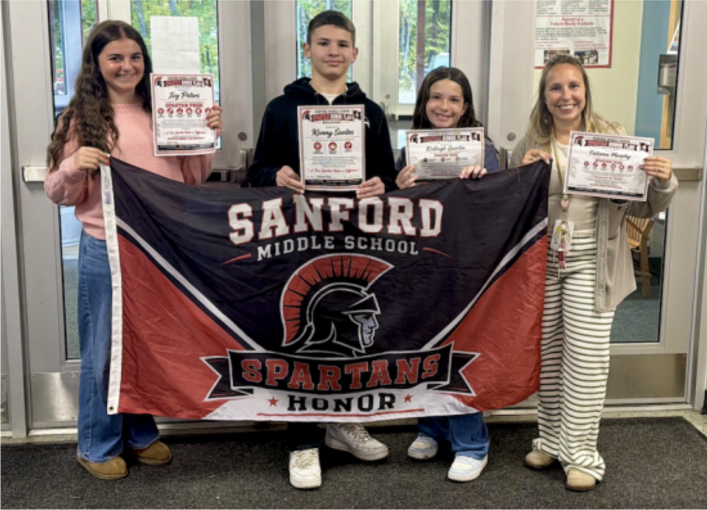 Four students raise a flag stating Sanford Middle School Spartans Honor