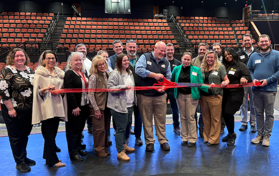 The Sanford Performing Arts Center (SPAC) officially became a member of the Sanford-Springvale Chamber of Commerce, marking the partnership with a morning mixer and ribbon cutting ceremony hosted on the theater's stage. The event gave local business leaders a chance to mingle, explore the facility, and get a behind-the-scenes look at what the Performing Arts Center has to offer. For many, it was their first time stepping foot inside. "I met a lot of new people who had never been to the Performing Arts Center," said Brett Williams, SPAC's Executive Director. "One of the things we like to do is offer tickets for first timers for meetings like this." That generosity extended to everyone in attendance. Williams offered a complimentary pair of tickets to any attendee who followed up, and the response was immediate. Chamber Executive Director Cari Quater, who also attended her first visit to the theater that morning, said a handful of people reached out right away to claim tickets for upcoming shows. "I had probably five or six people get back to me right away saying, 'I'd love to see this show, I'd love to see that show,'" she said. "It was a really good opportunity, which is what we want. We want people to have that exposure to the theater." A highlight of the event was a backstage tour, where guests got an up-close look at the sets, costumes, and technical equipment currently in place for the center’s upcoming production of Newsies. Williams walked attendees through the theater's fly system, moving lights, and ongoing equipment upgrades, details that left a visible impression. "They were all wide-eyed, like kids," Williams said. "Because unless you're backstage, you don't know what all goes on." For Williams, the Chamber membership is about more than visibility. It's about building an ecosystem where local businesses and the arts can support each other. SPAC is already a member of the Kennebunk-Kennebunkport-Arundel Chamber of Commerce, and joining the Sanford-Springvale chapter deepens those local ties. "The performing arts center exists to bring art to the community, but also give opportunities for businesses in the community so we can be an economic driver for them," he said. Quater echoed that sentiment, noting the Chamber plans to add a "Things to Do" tab to its website with SPAC prominently featured, so residents and visitors can easily find upcoming shows. She also noted that Williams has appeared on two local radio programs, York County Conversations and York County Connect on Seacoast Oldies, as part of broader efforts to raise awareness about what the theater offers. "When people think, 'What is there to do in Sanford?' they'll be able to find it immediately," she said. For Williams, the biggest win isn't the ribbon cutting. It's what comes next. "The biggest win is when you come to see one of our performances, and then your wheels really start turning about what this is for the community. It’s about how we can all work together to make even greater things happen."