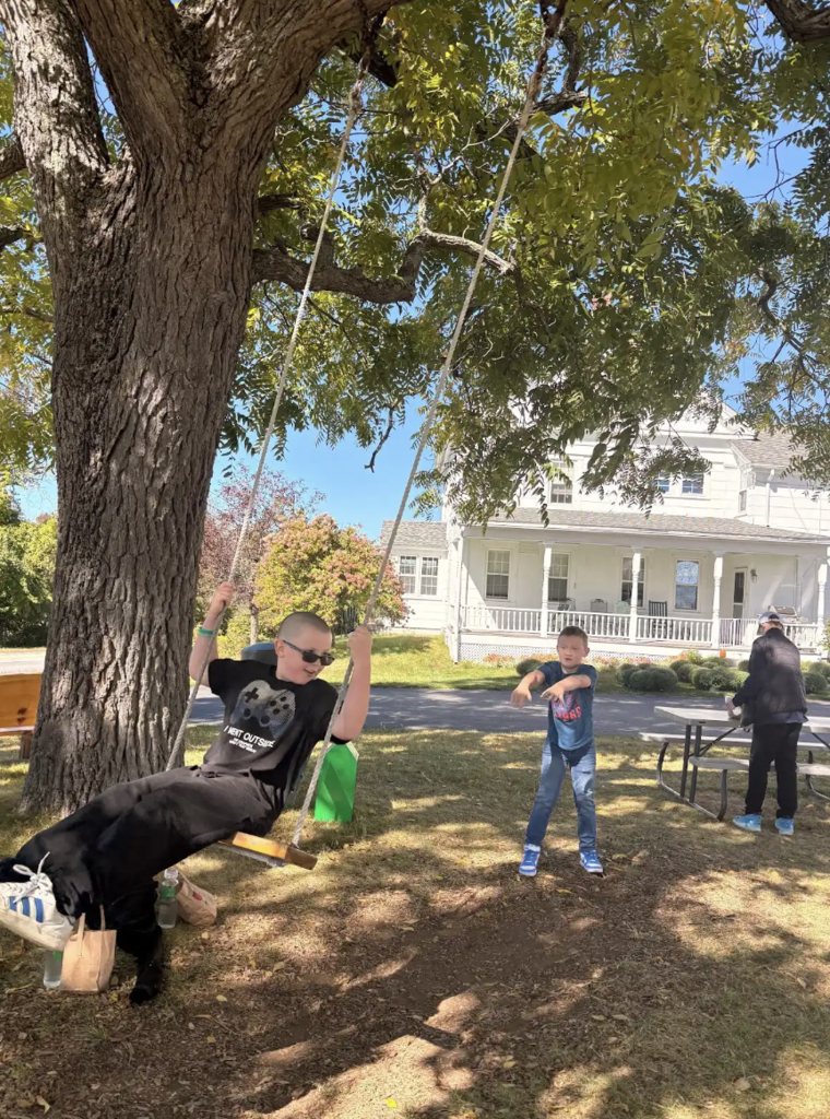 One student swings on a swingset while another student pushes him.