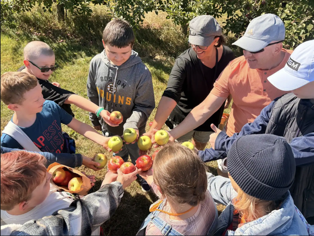 Staff and students stand in a circle and raise their apples in the middle.