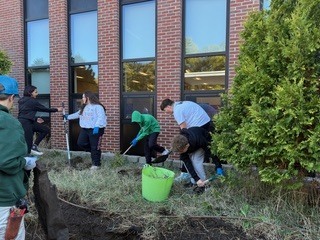 A group of students rake and weed together.