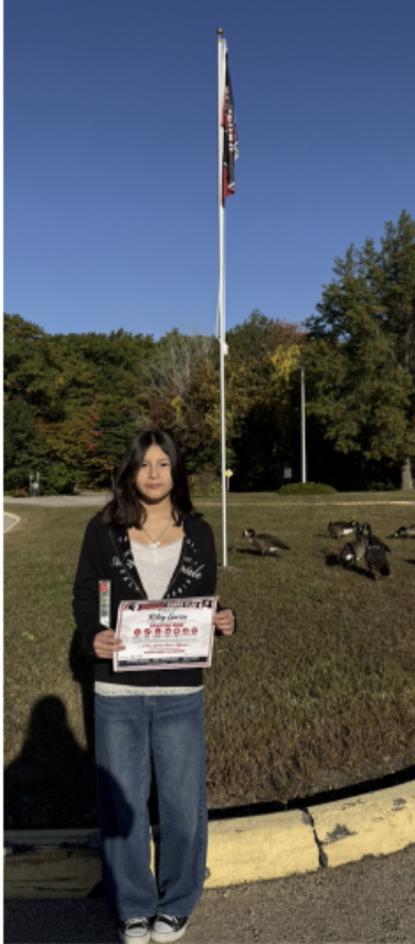 One students poses with her certificate in front of the flag pole.