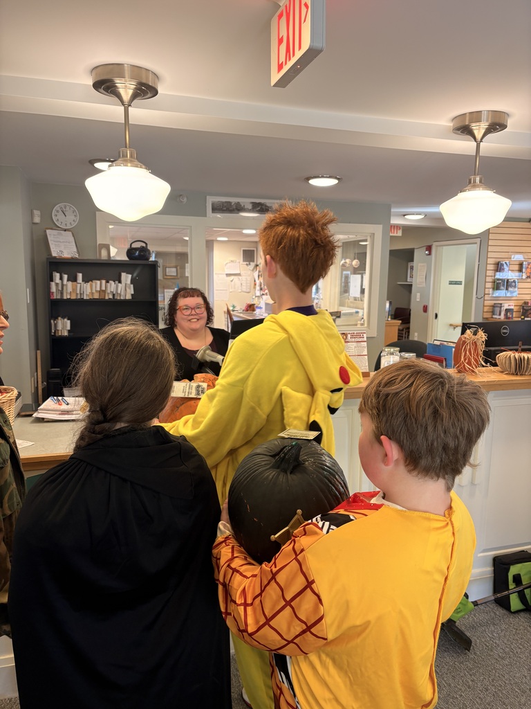 Three students present a pumpkin to a woman at the library.
