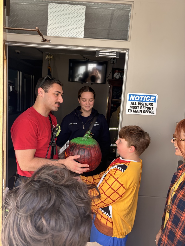 A student hands a pumpkin to two firefighters.