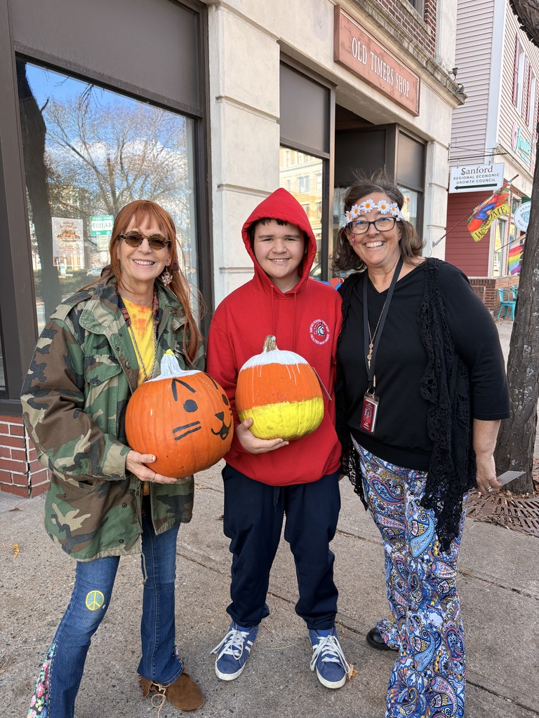 Two women pose with a student holding two pumpkins.