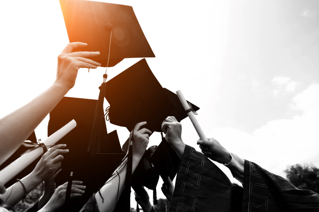 A group of people in graduation attire, holding up caps in the air, in front of a bright sky.