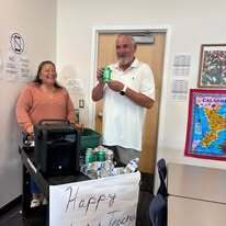 A man and woman stand in a room with a banner that says "Happy" next to a table with drinks.