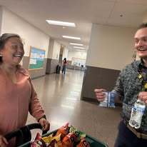 Two people smile, one holding snacks in a basket, the other holding a water bottle and paper.