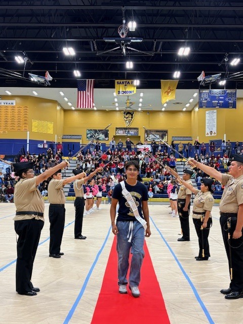 A student walks on a red carpet in a gymnasium with marching band members and police.
