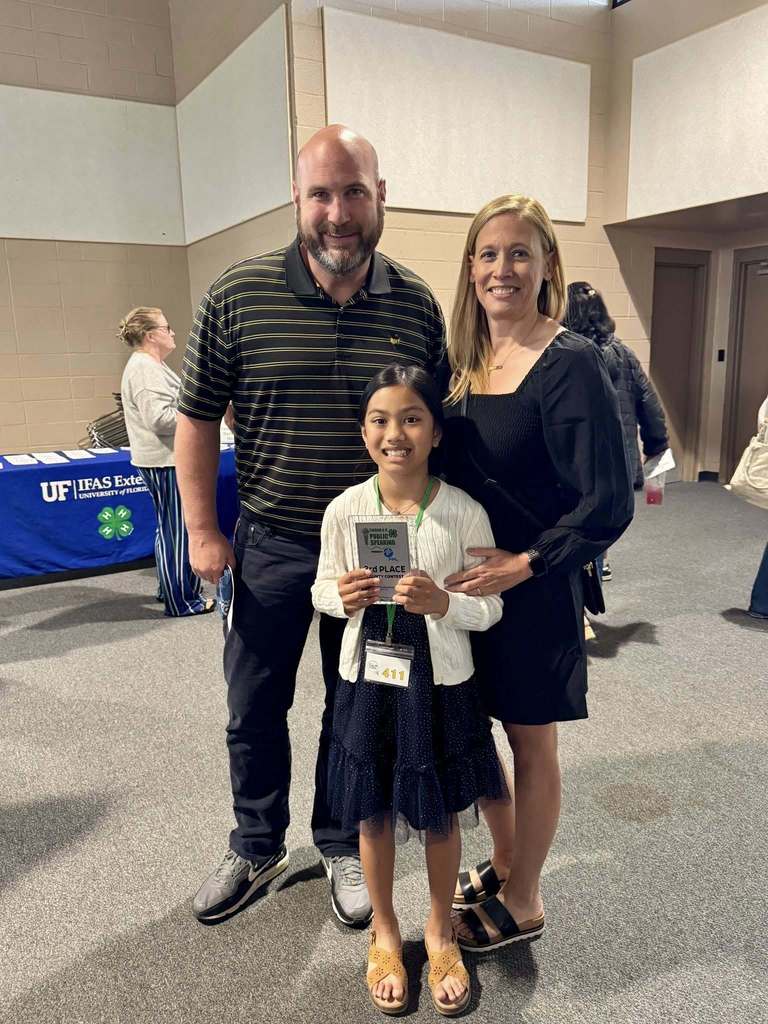 Mikaela standing with her teachers, Mr. Mathes and Mrs. Nelms; smiling and holding her award.