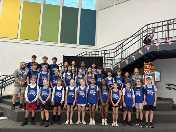 East Bay Middle School Cross Country team members and coaches pose together inside the school, wearing blue team uniforms and smiling for a group photo.