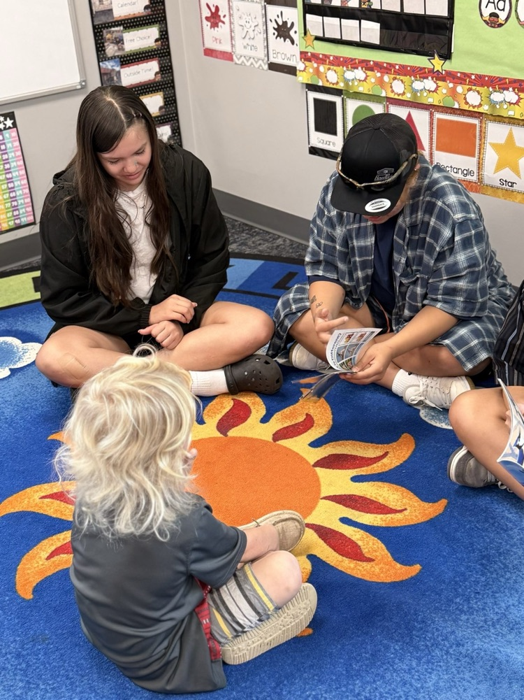 volleyball students sitting on the carpet reading to our headstart students