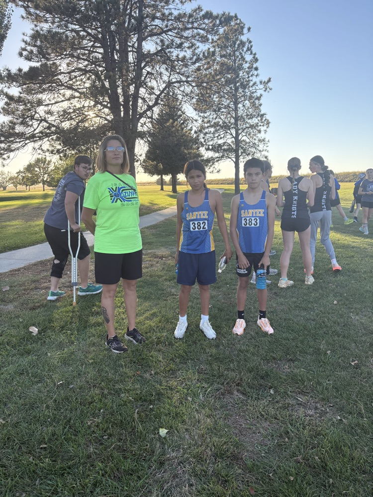 picture of two students in their blue cross country jerseys and their coach with a green tshirt on at the cross country meet