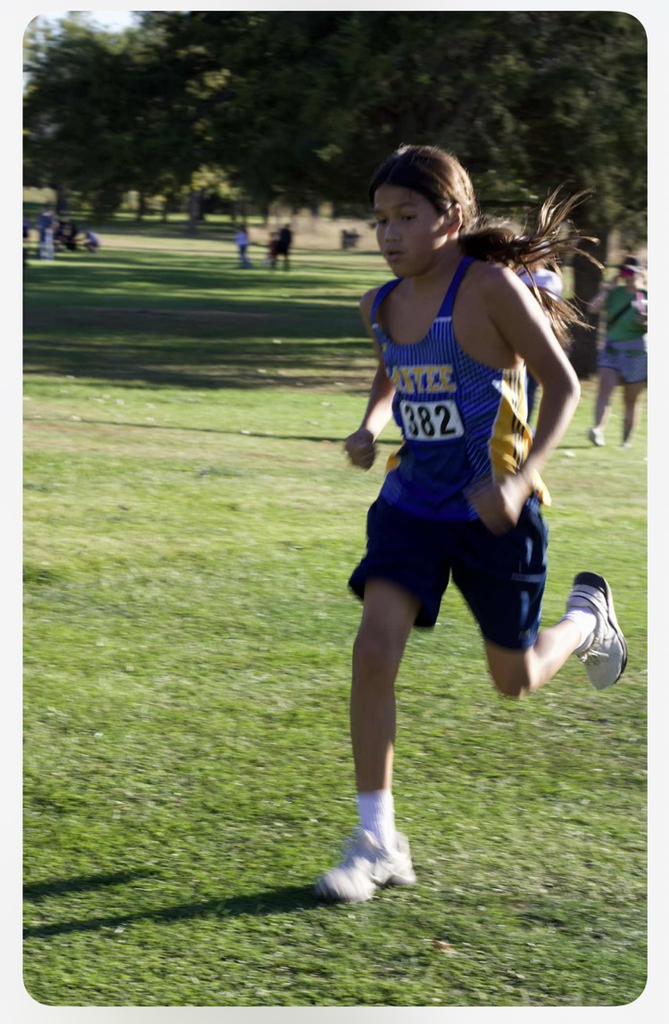 picture of our cross country athlete running on grass with his blue jersey on