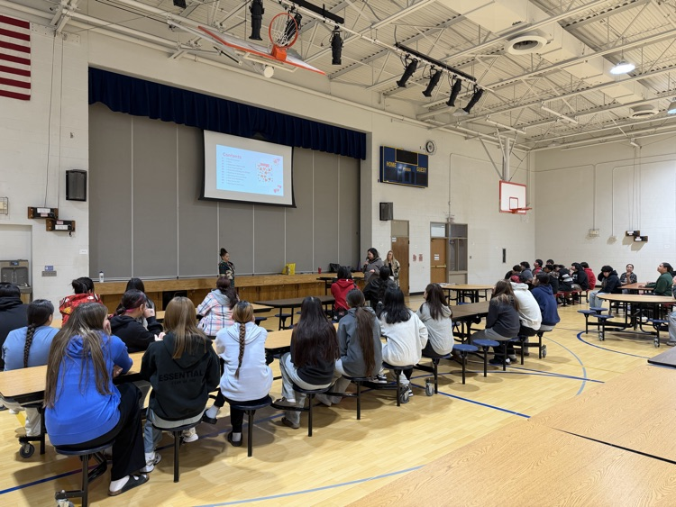 Photo of students sitting at tables listening to a presentation.