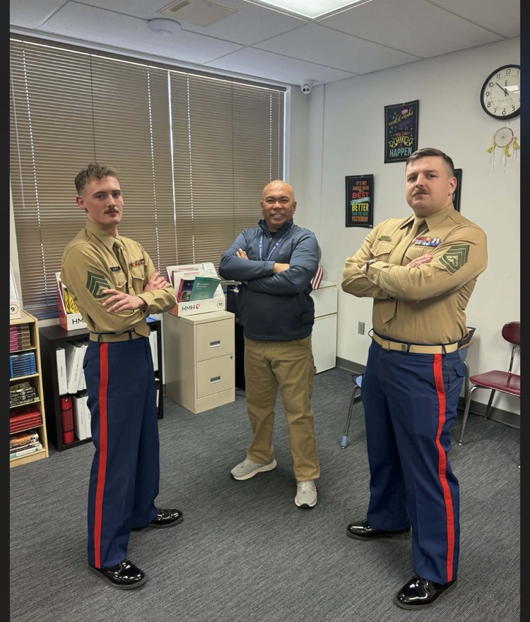 a teacher and two gentlemen standing in a classroom with their military uniforms on