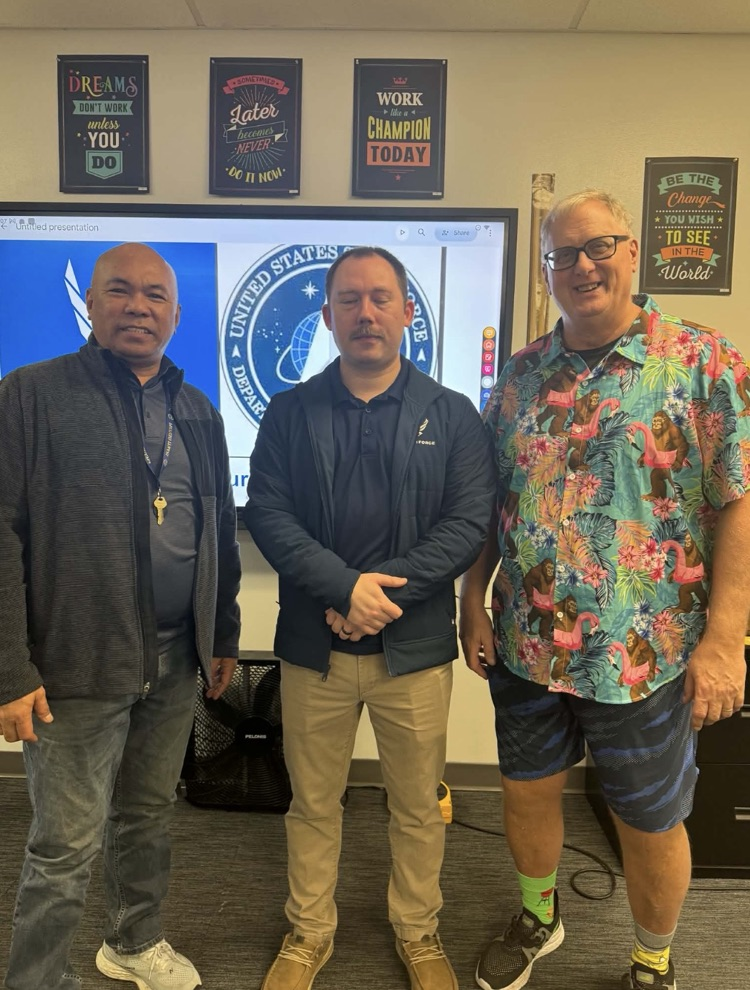 a teacher and two gentlemen standing in a classroom with their military uniforms on