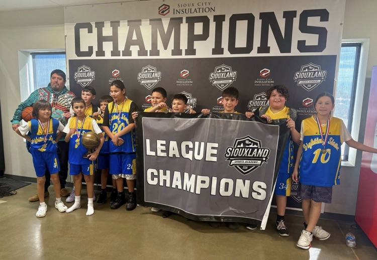 Pee wee basketball players in blue jerseys holding a black and white league champions poster and a trophy