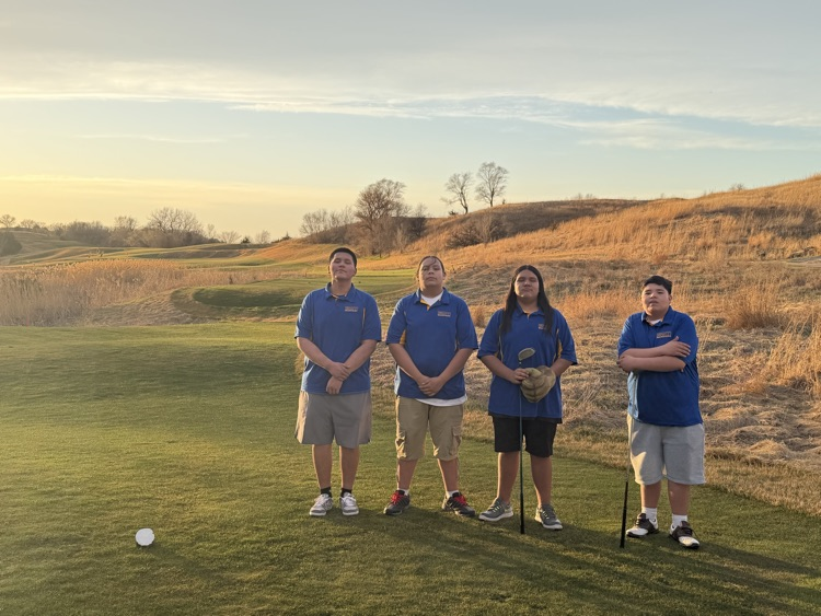 Photo of 4 male golfers in their blue golf shirts on a green golf course. 