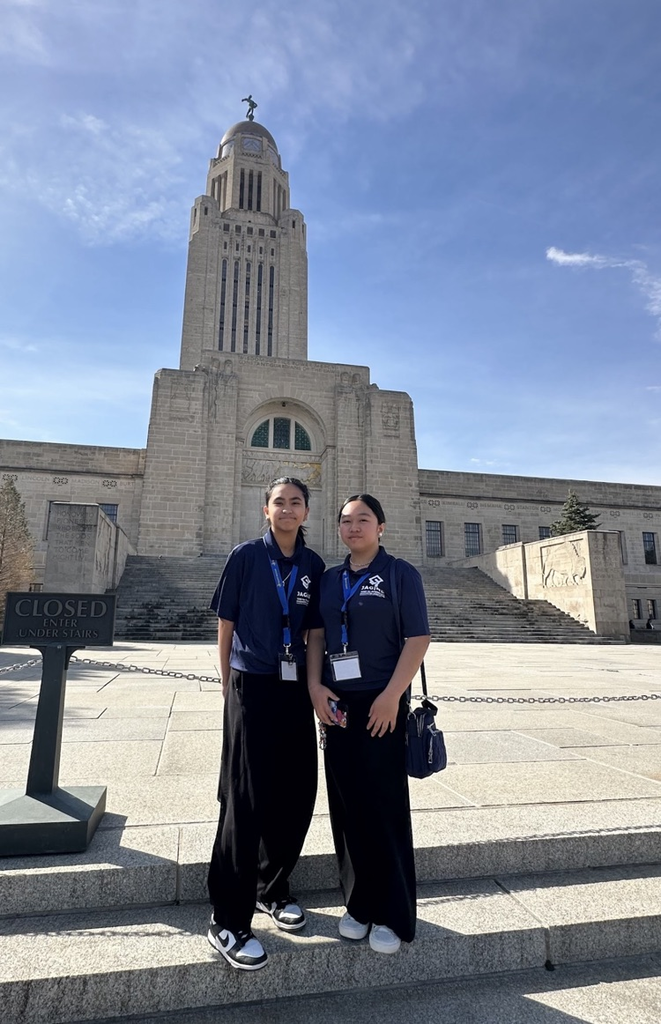Two female students dressed in all black standing on concrete steps in front of the Nebraska state capitol building 