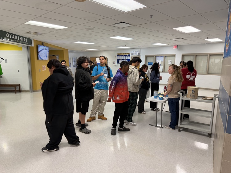 students standing in line at a folding table to put toppings in their ice cream. 