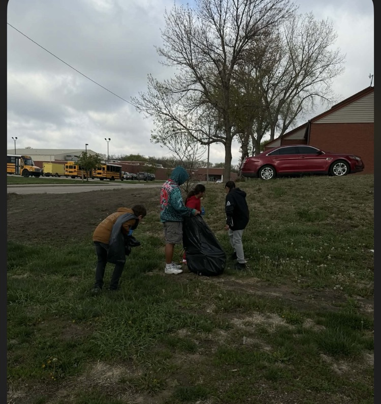 Photo of one para and 3 students picking up trash outside the school building.