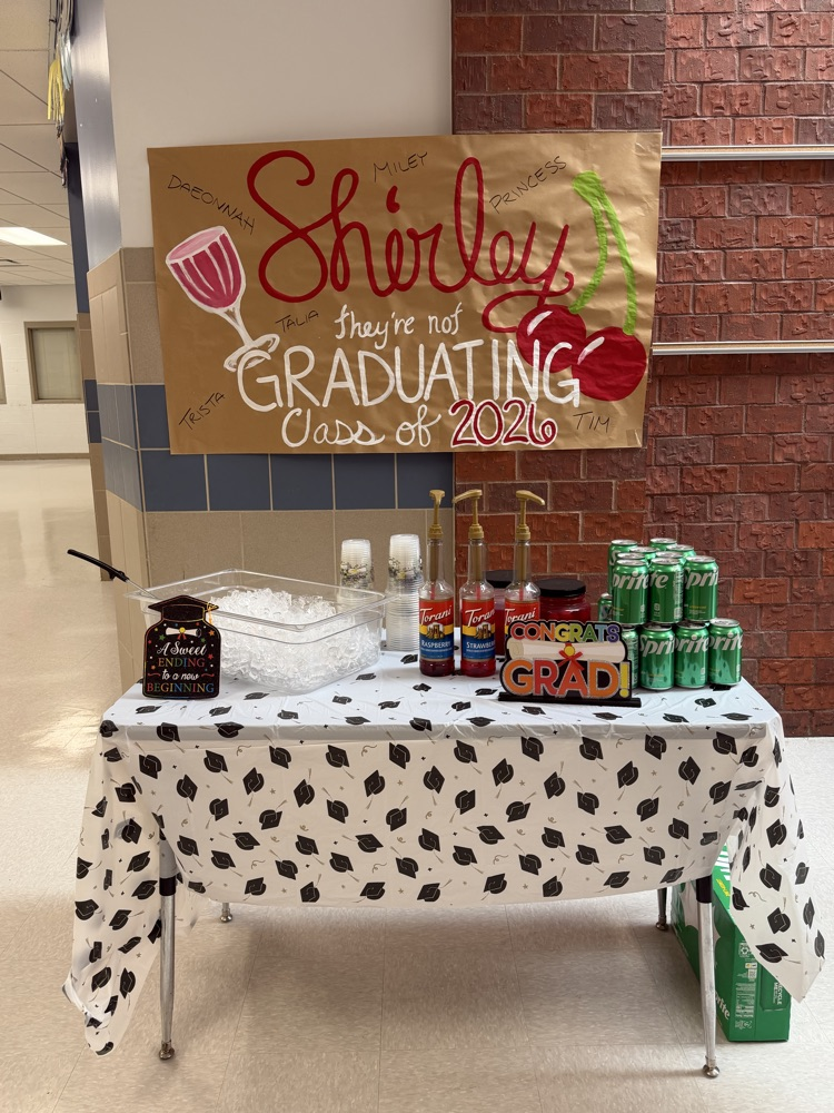 Image of a table with a white tablecloth in front of a brown sign that says surely they are not graduating