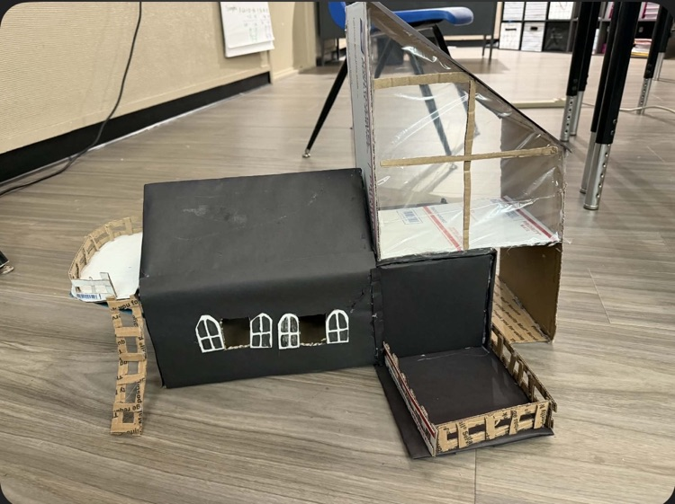 Photo of the middle school math project- building houses out of recycled materials. black house