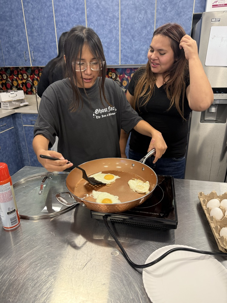 Two students practice frying eggs during a Family and Consumer Sciences cooking lesson.