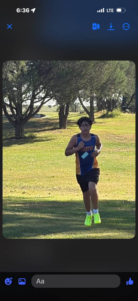 photo of student in a blue running uniform running on grass in a cross country meet 