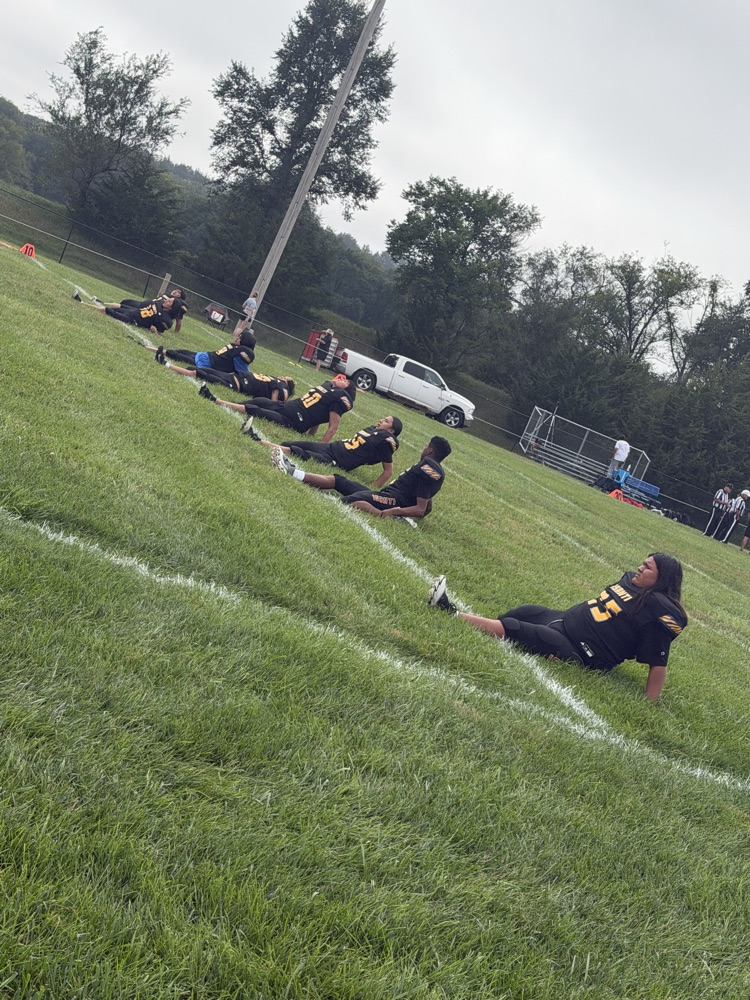 Isanti football team in black jerseys doing stretches on the field 