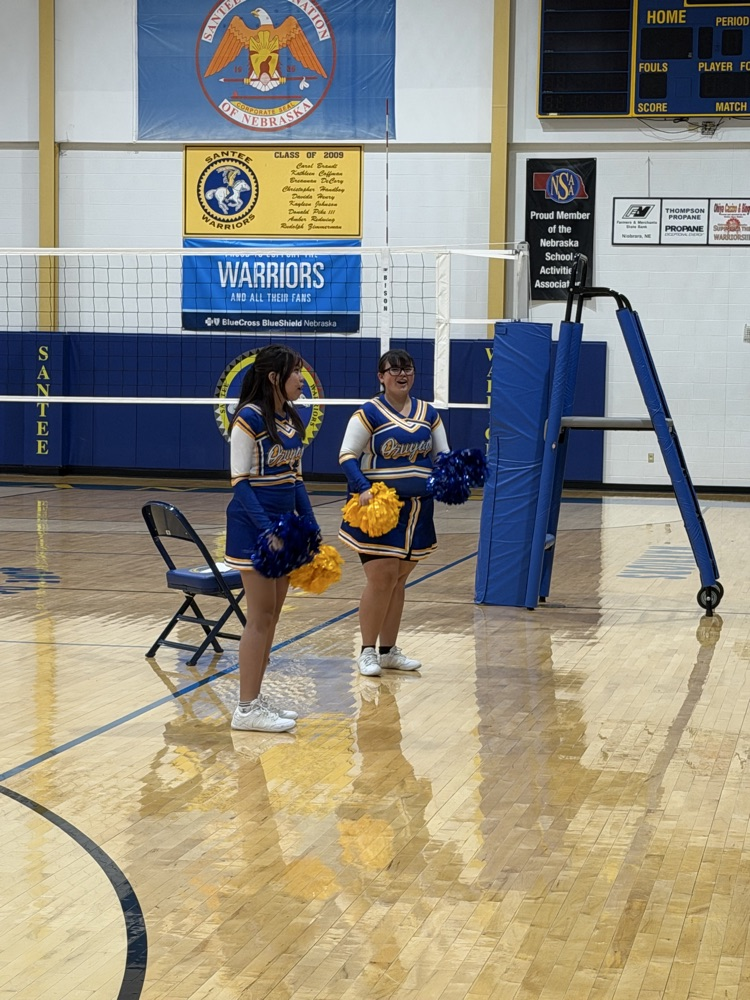 2 isanti cheerleaders in blue uniforms standing on the basketball court 