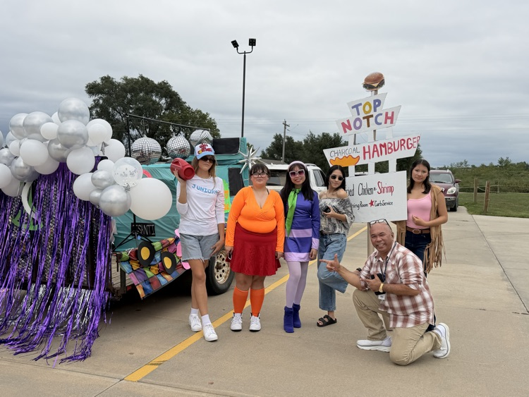 students in 70s costumes posing for a picture by a parade float 