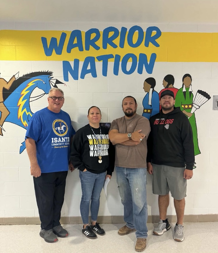 photo of 4 individuals, 1 female & 3 males posing in front of a white wall with blue letters that say Warrior Nation