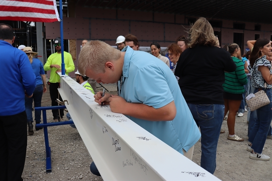 Student signs the final beam to be placed atop the new high school 