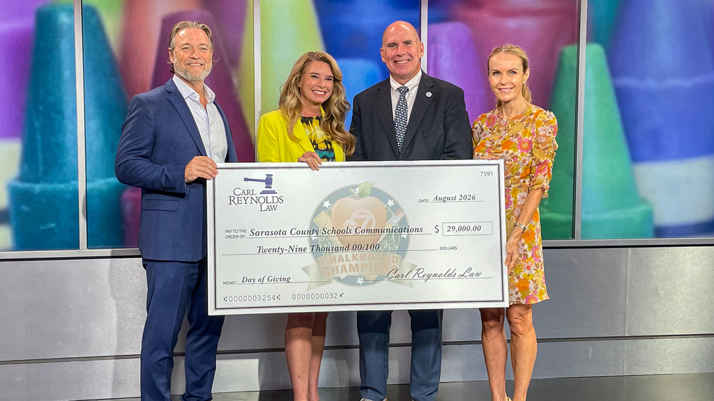 Four adults holding a large check with a logo and text. A colorful background is behind them.