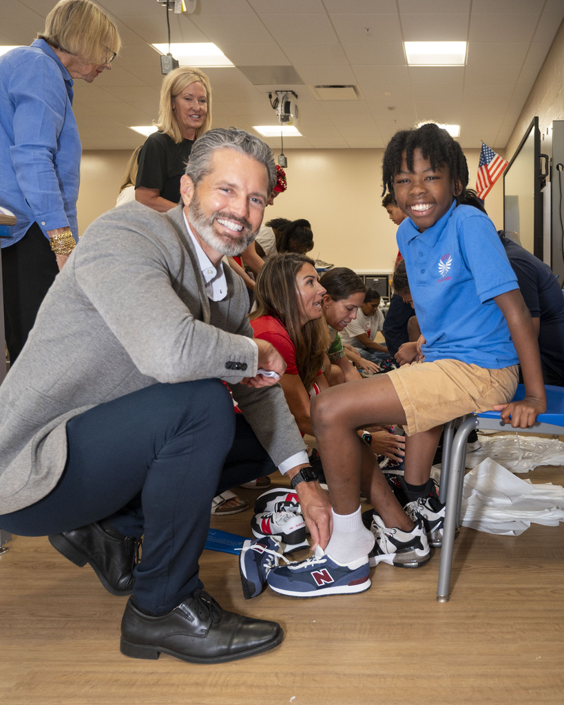 Superintendent Terry Connor kneels next to a boy in a blue shirt and shorts.
