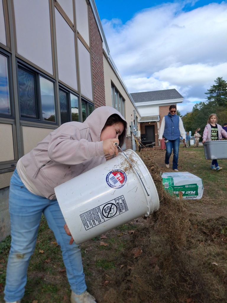 A student pouring soil into the garden bed while other students and educators carry soil.