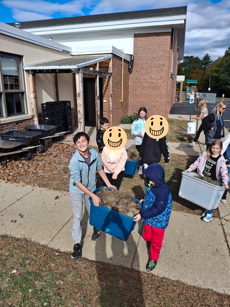 Second and seventh grade students smiling for the camera while carrying soil.