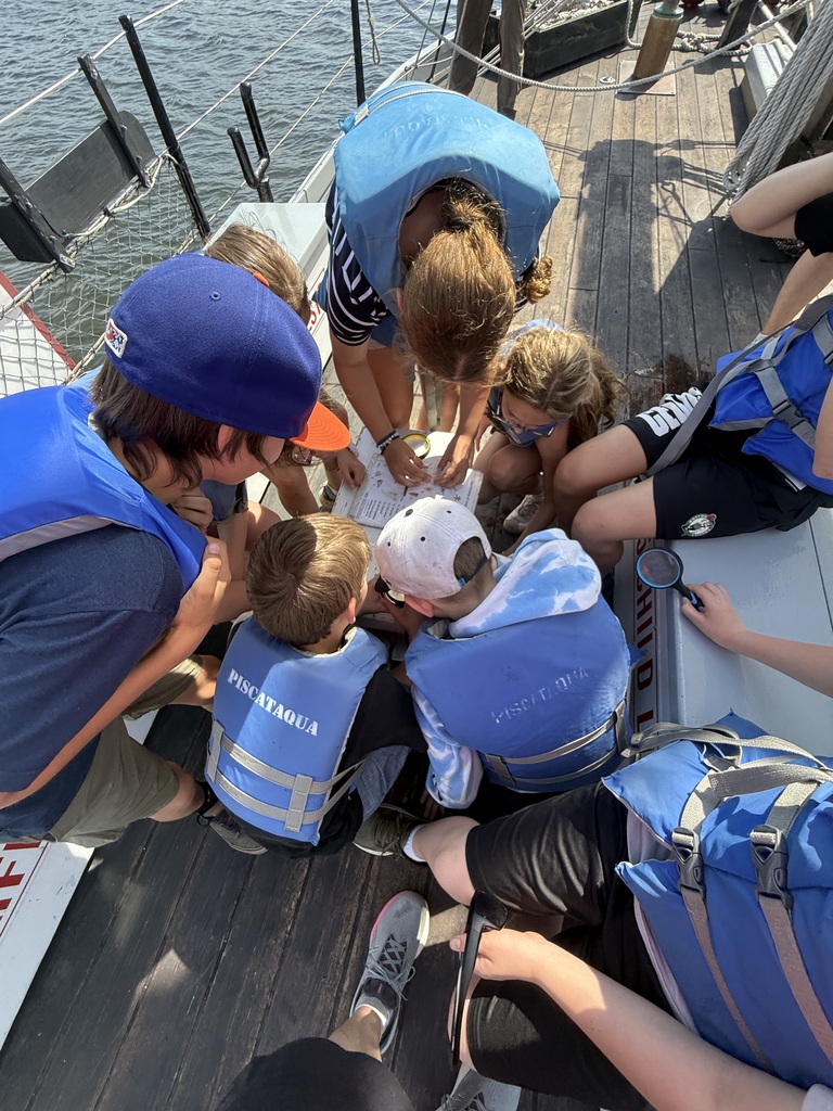 A group of students with lifejackets on sitting in a circle on the deck, observing plankton.