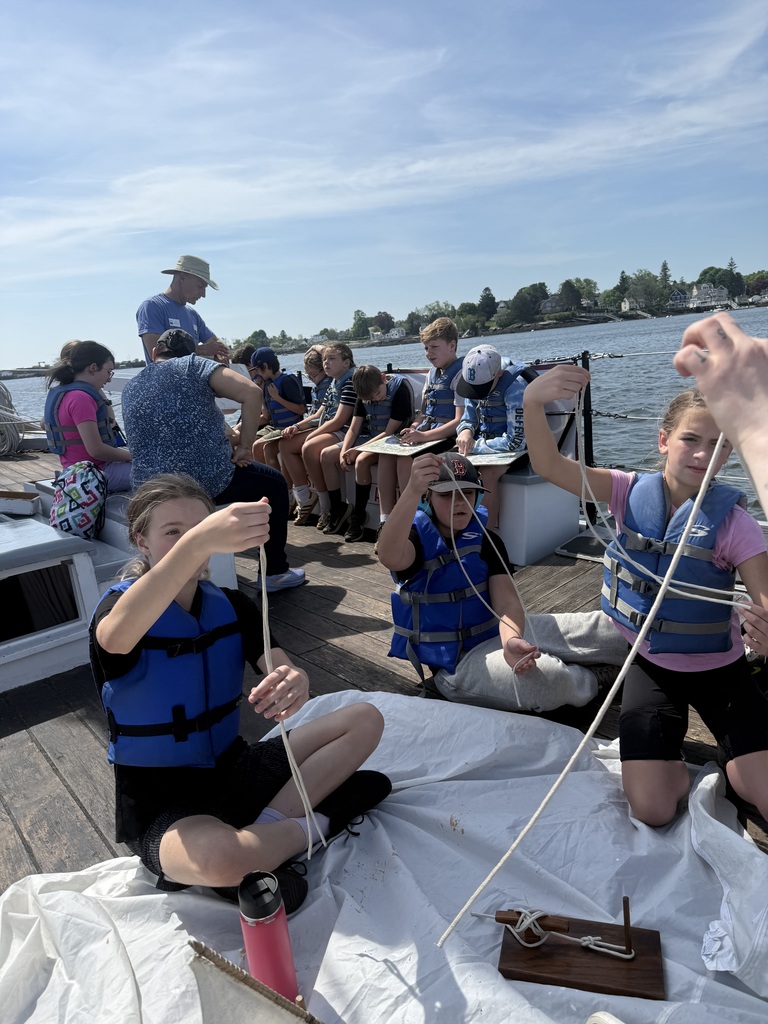 Students working to tie knots and fold the sail.