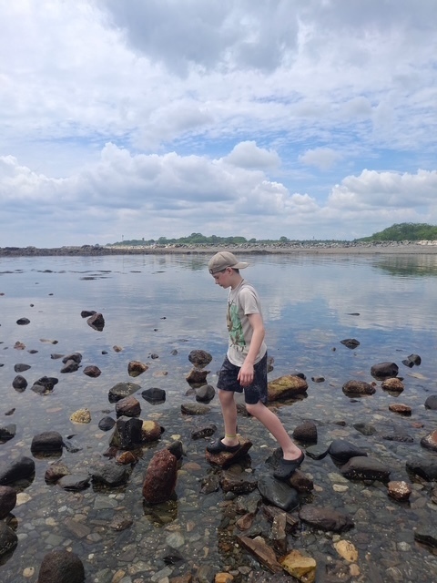 A student with a backwards cap stepping across the tide pool rocks