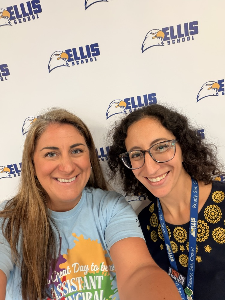 Ms. Perkins and Mrs. Rosenberg smiling in front of a banner 