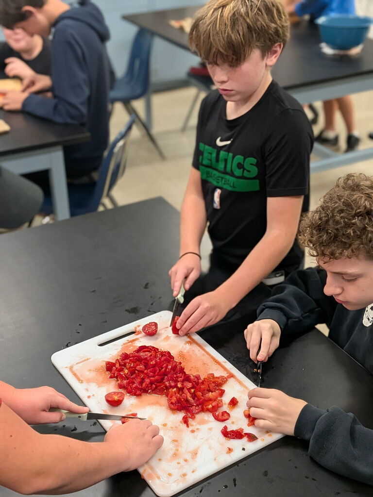 Three students cutting up tomatoes for salsa