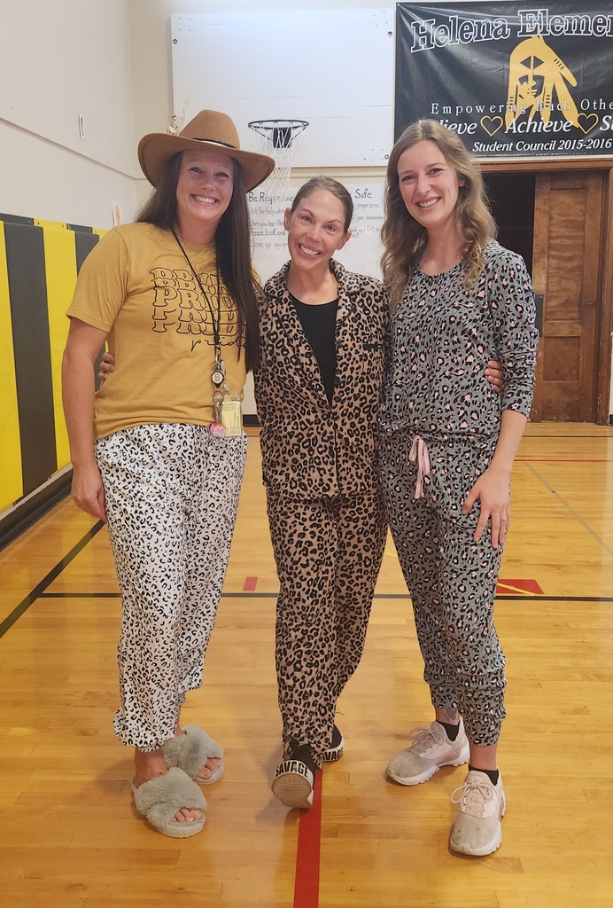 Three women posing together in a gym. They are dressed in leopard print pajamas and slippers or sneakers, with one wearing a school shirt and cowboy hat.