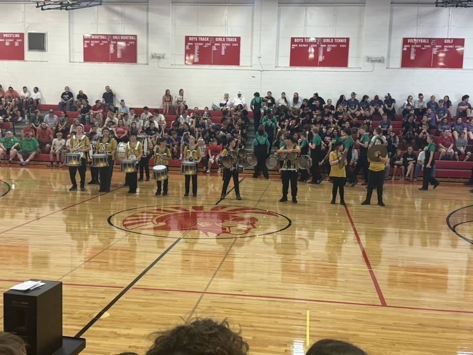 picture of middle school drumline students stanging at the ready in front of packed bleachers.