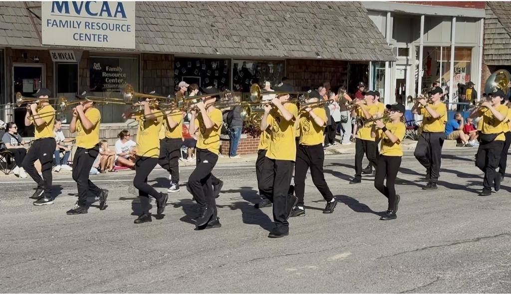 middle school students in black pants and gold t-shirts play their horned instruments while marching in a parade.