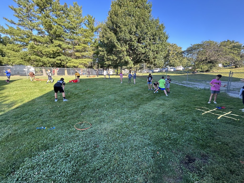 Large group of students spread out on a grassy field playing various outdoor games.
