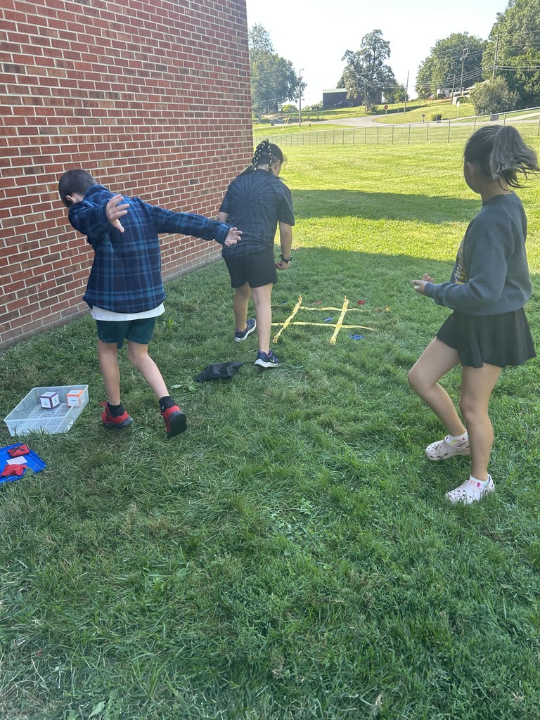 Three students toss beanbags into a tic-tac-toe grid laid out on the grass.